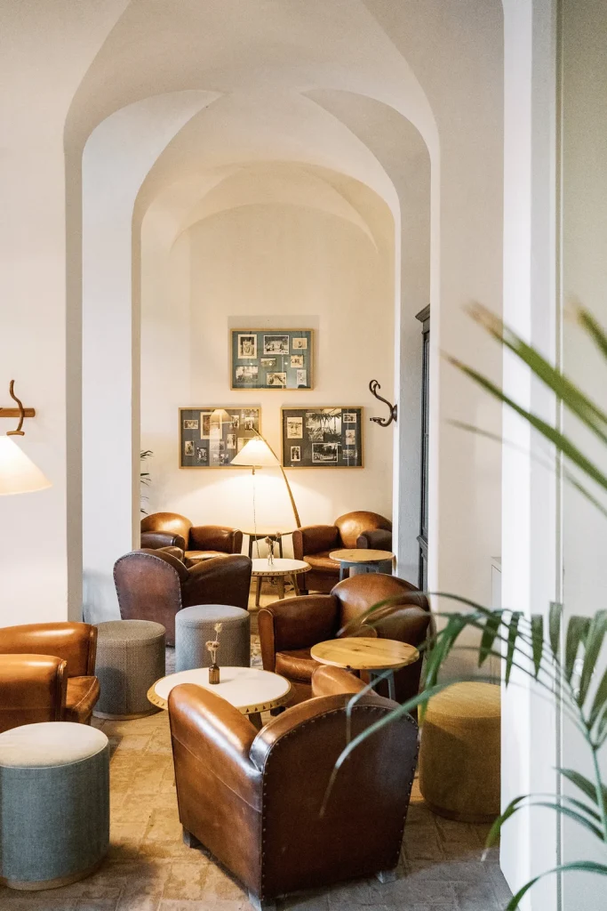 A cozy lounge area with warm leather armchairs, soft lighting, and vintage framed photographs on the walls. The arched ceiling and neutral tones enhance the inviting and nostalgic ambiance of this rustic setting.