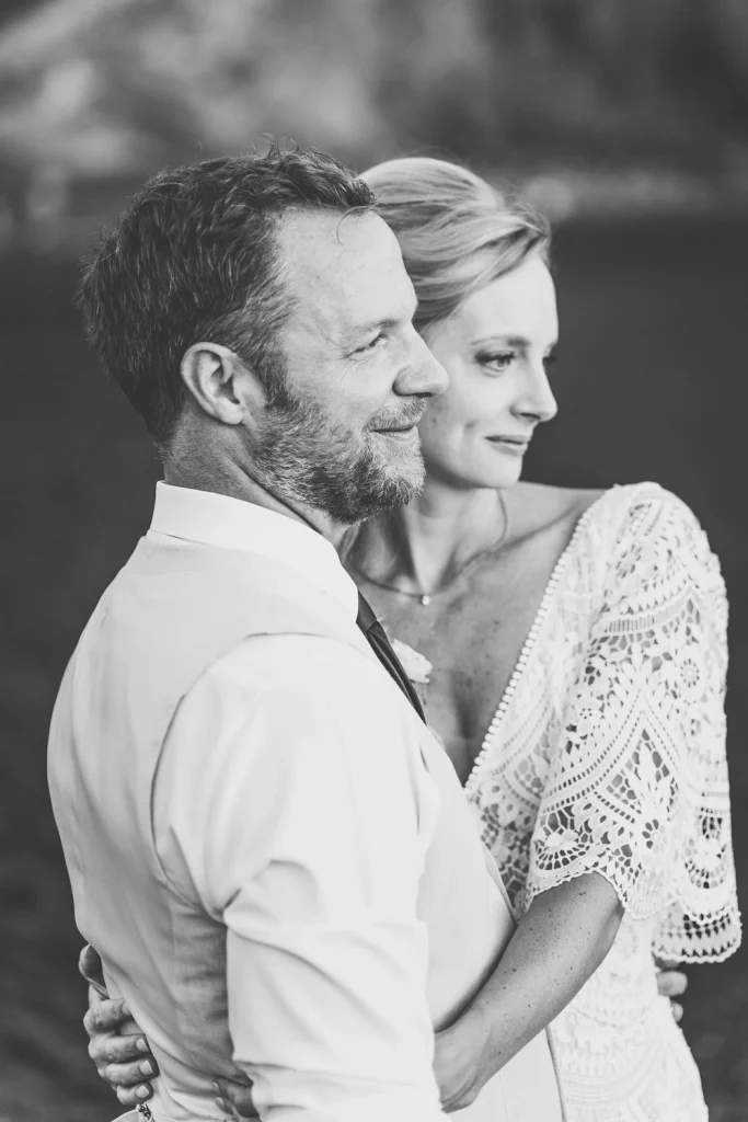A black and white close-up portrait of a newlywed couple embracing, with the bride gazing into the distance and the groom smiling contentedly.