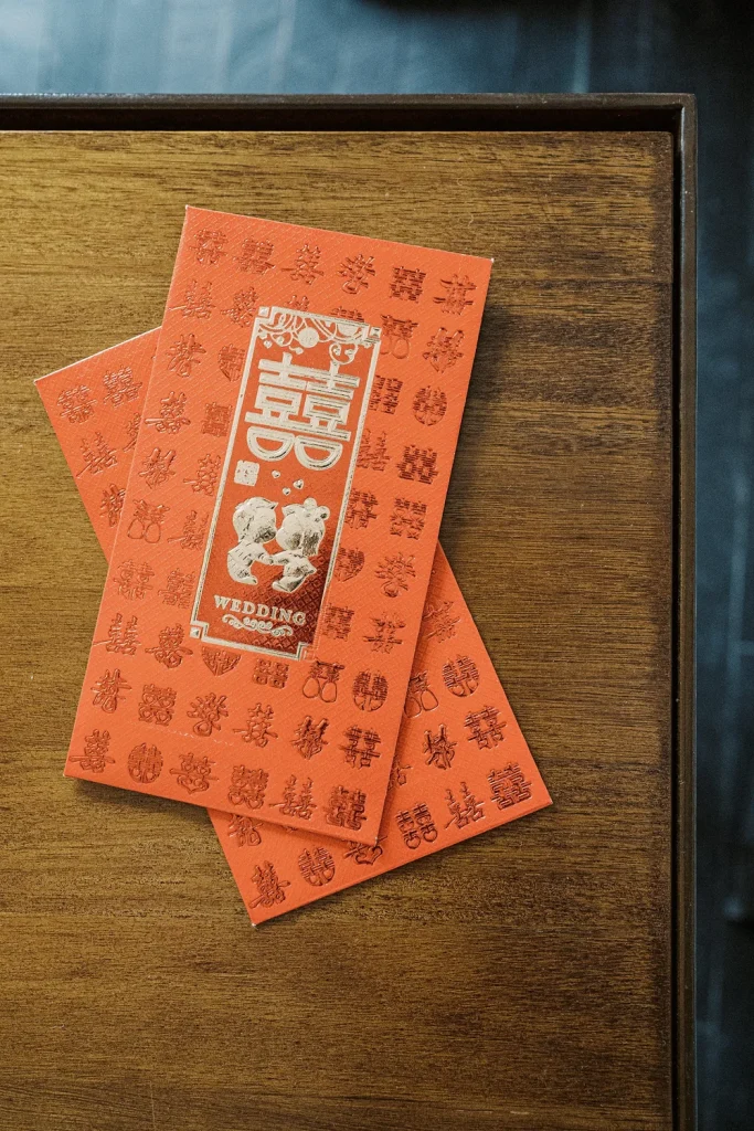 A traditional red Chinese wedding envelope with gold embossed double happiness symbols, placed on a wooden table.