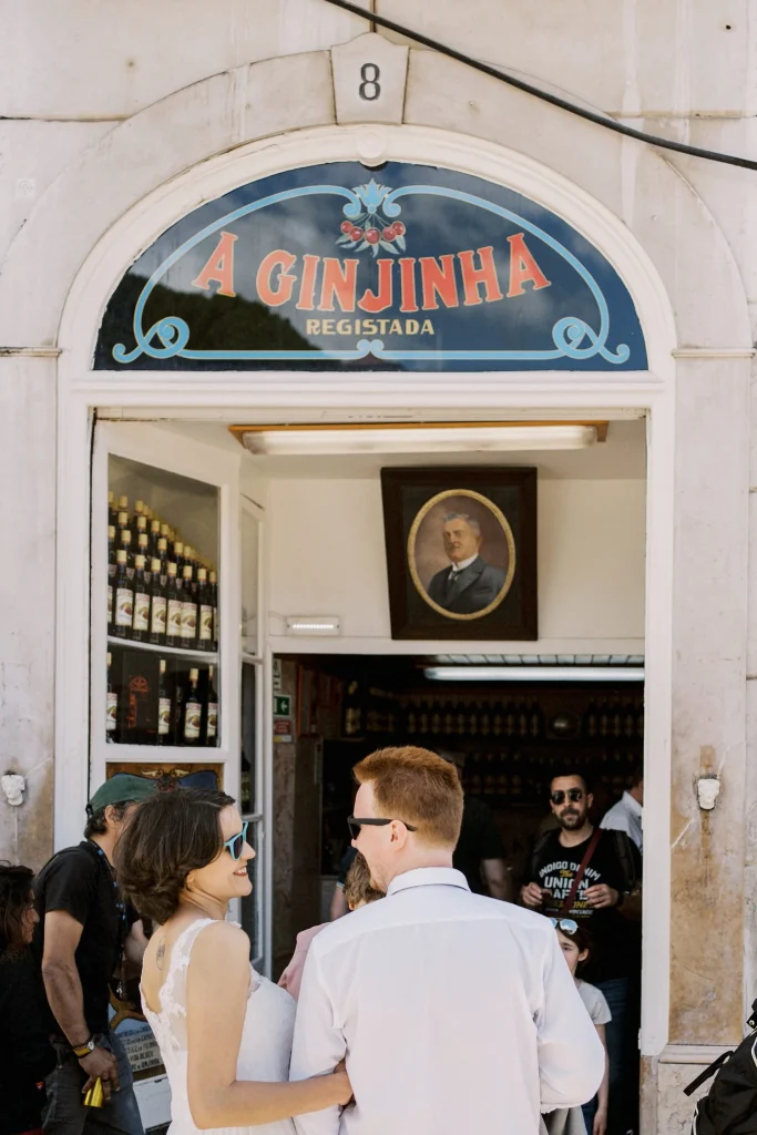 A lively scene outside a traditional Lisbon ginjinha bar, with people chatting and a bartender serving cherry liqueur.