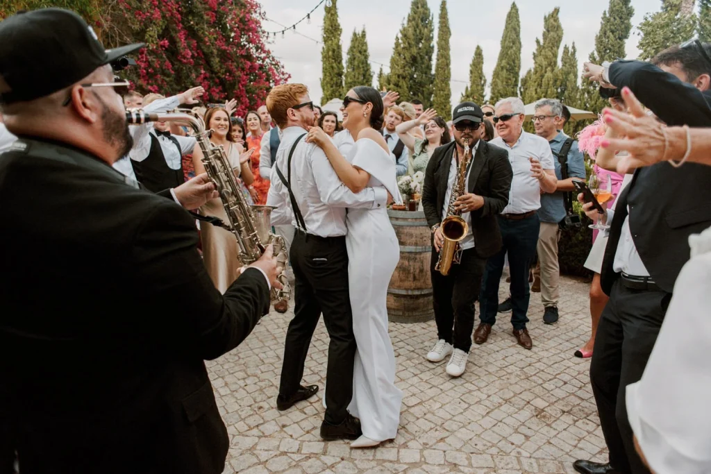 A newlywed couple shares their first dance outdoors as a live jazz band plays, with guests clapping in celebration.