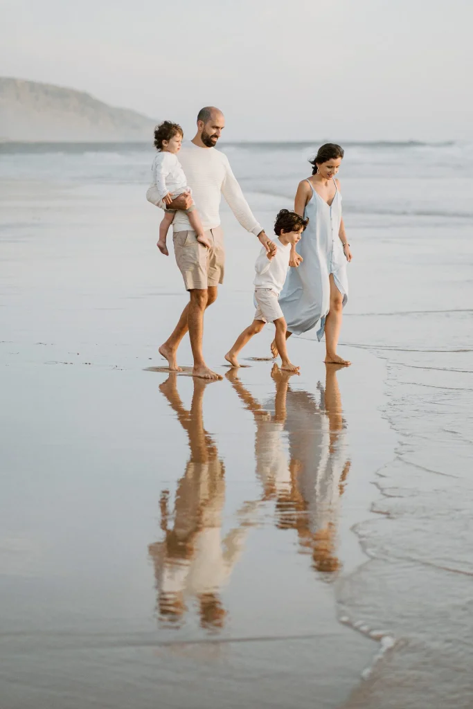 A family walks along the shoreline, their reflections visible in the wet sand as the waves roll in.