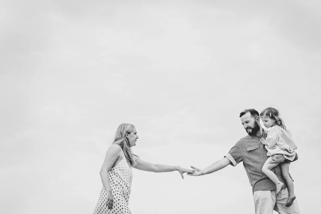 A black and white artistic shot of a couple reaching out to hold hands with a blurred background.