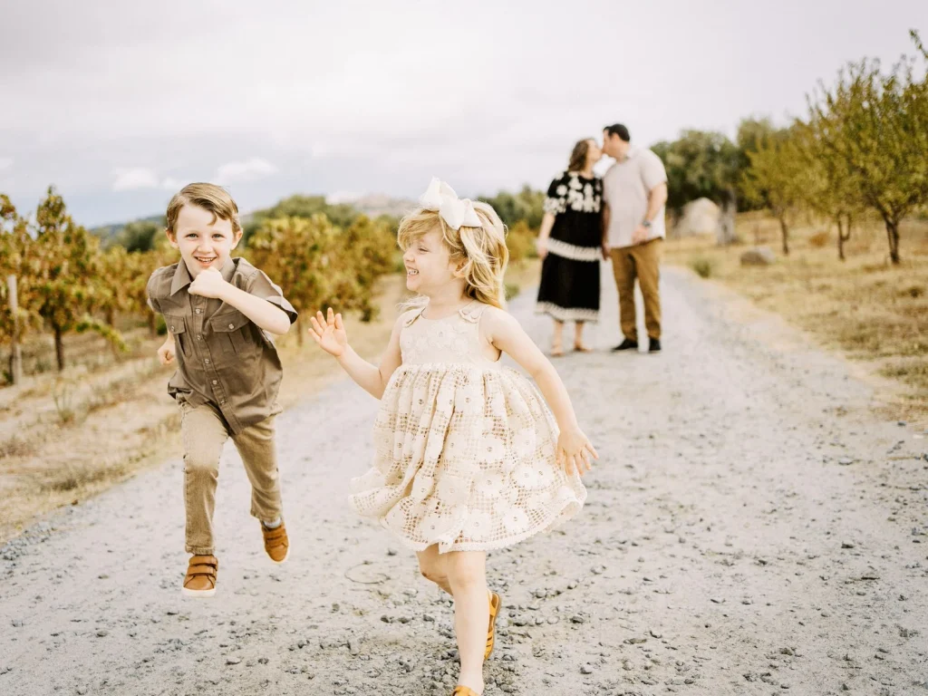 Young children running joyfully along a dirt path, with blurred adults in the background.