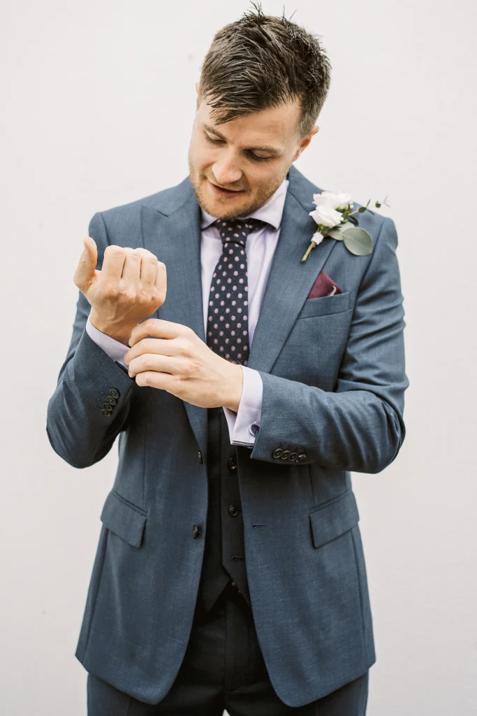 Groom adjusting his cufflinks in a navy suit with a white boutonniere.