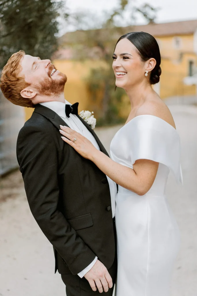 A bride and groom share a joyful laugh, with the groom tilting his head back in laughter.
