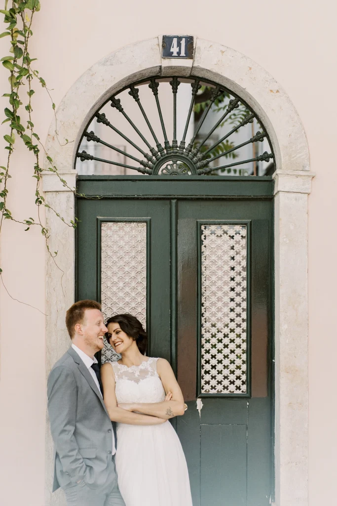 A newlywed couple shares a joyful moment in front of a grand green door with intricate glass panels.