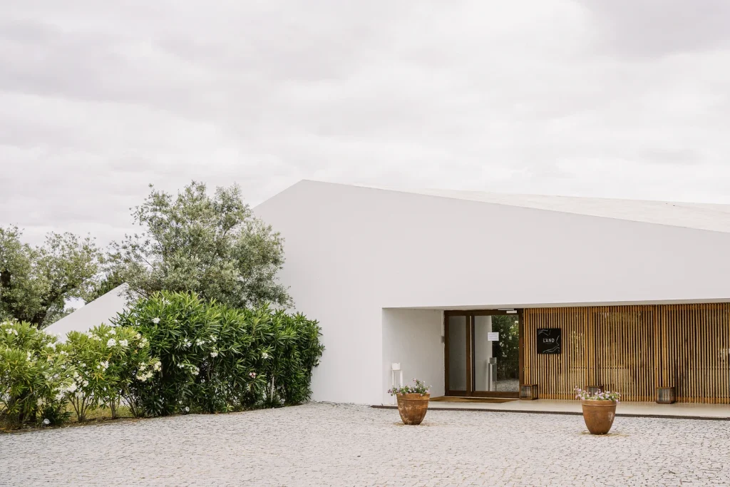 A contemporary wedding venue with minimalist white architecture, wooden paneling, and lush greenery at the entrance, creating a serene and elegant atmosphere.