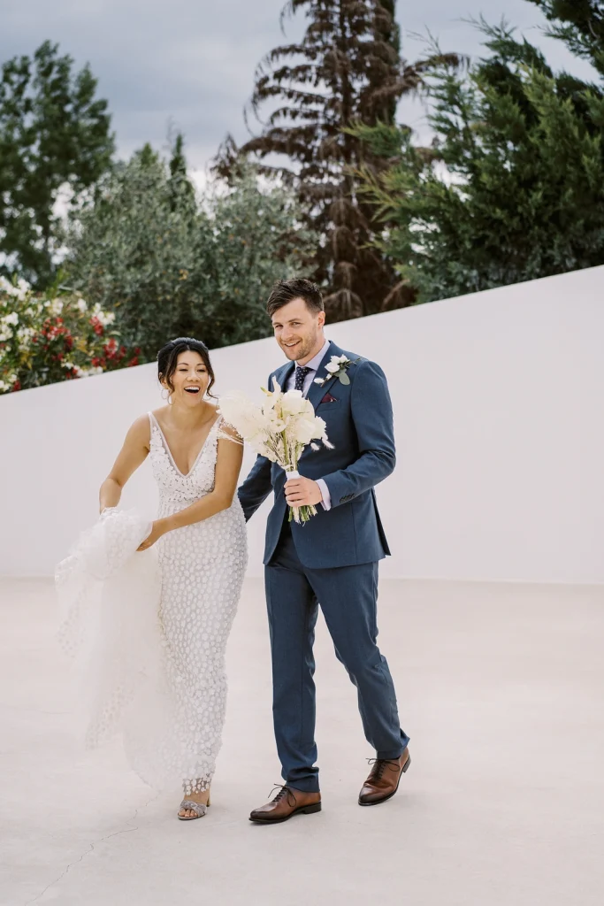 Newlywed couple walking happily together, bride holding bouquet and lifting her dress.