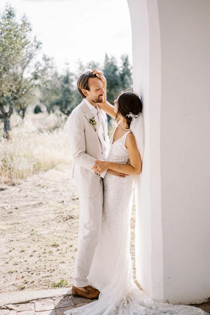 A newlywed couple shares a tender moment, embracing near a sunlit archway.