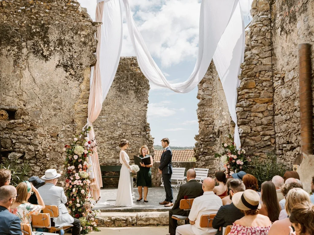A wedding ceremony set against the backdrop of ancient stone ruins, draped with flowing white fabric.