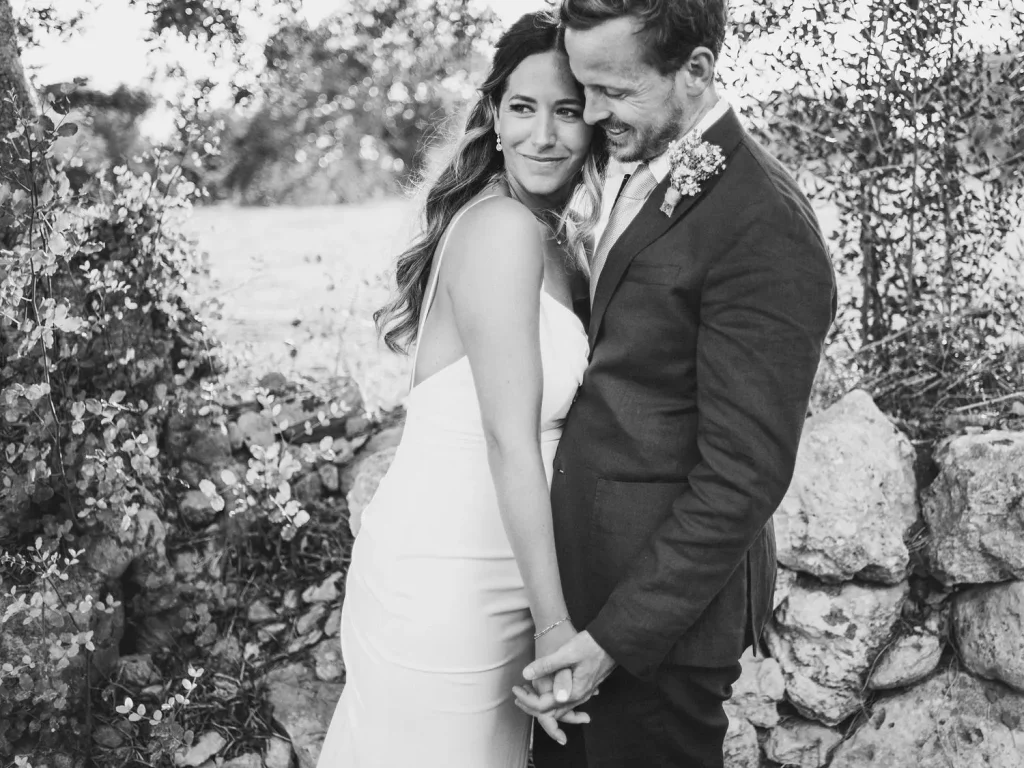 A bride and groom embrace, smiling as they lean into each other in a timeless black-and-white portrait.