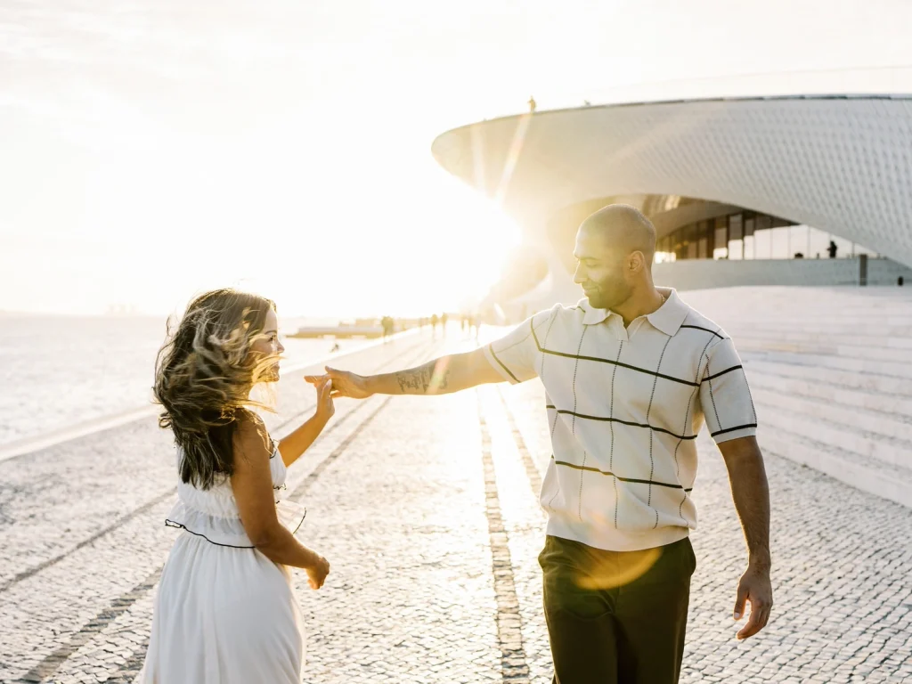 A couple dances at sunset near a modern architectural structure, bathed in golden light.