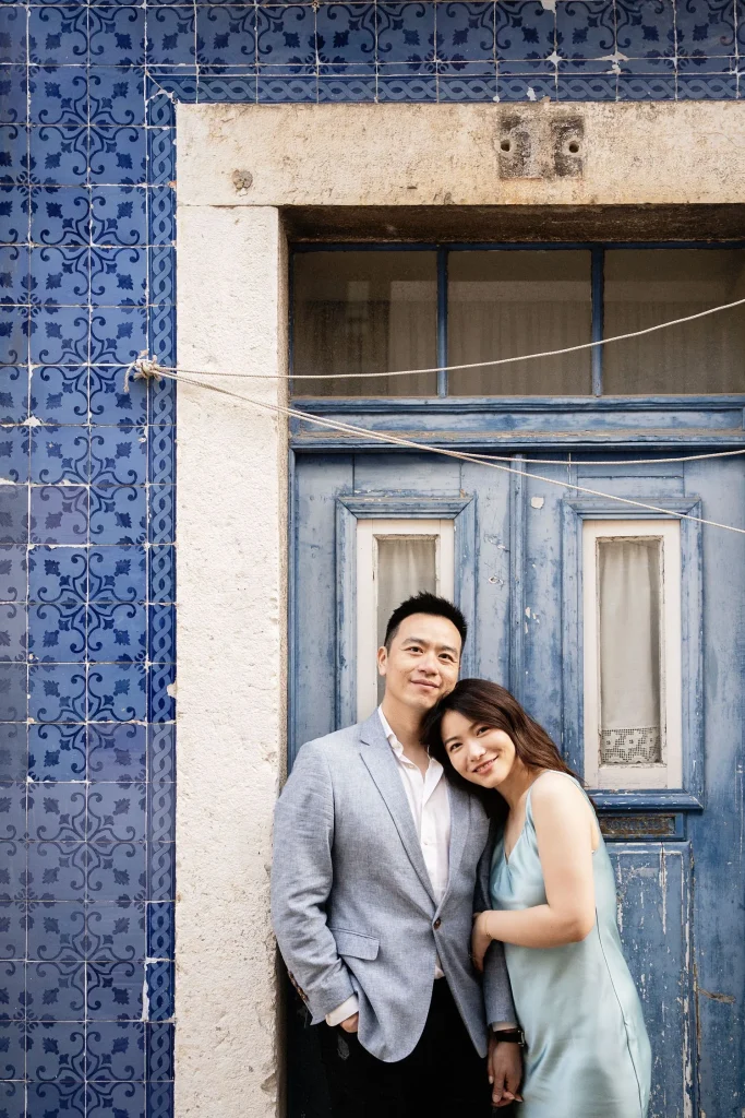 A couple poses in front of a rustic blue door adorned with traditional Portuguese azulejo tiles.