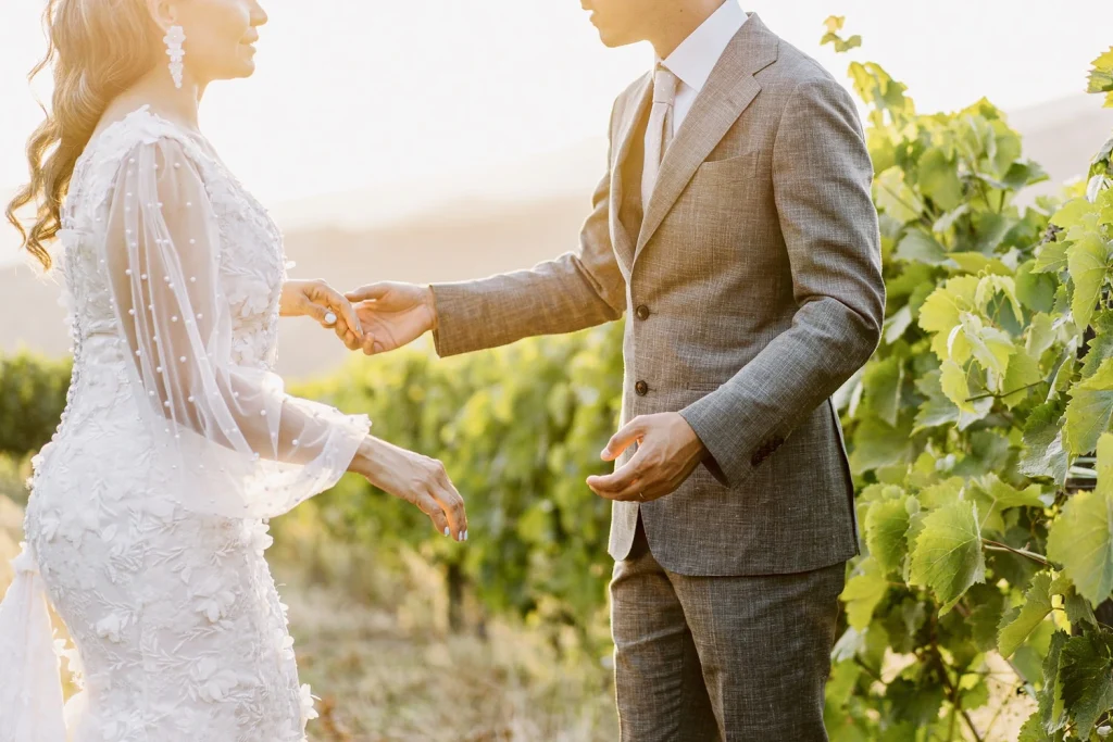 A bride and groom holding hands in a vineyard at sunset, with warm golden light illuminating their moment.