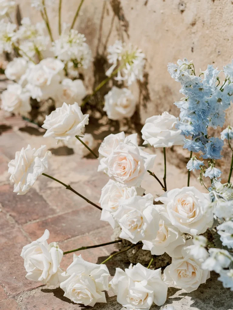 Close-up of white roses and blue flowers arranged along a rustic stone wall for a wedding.