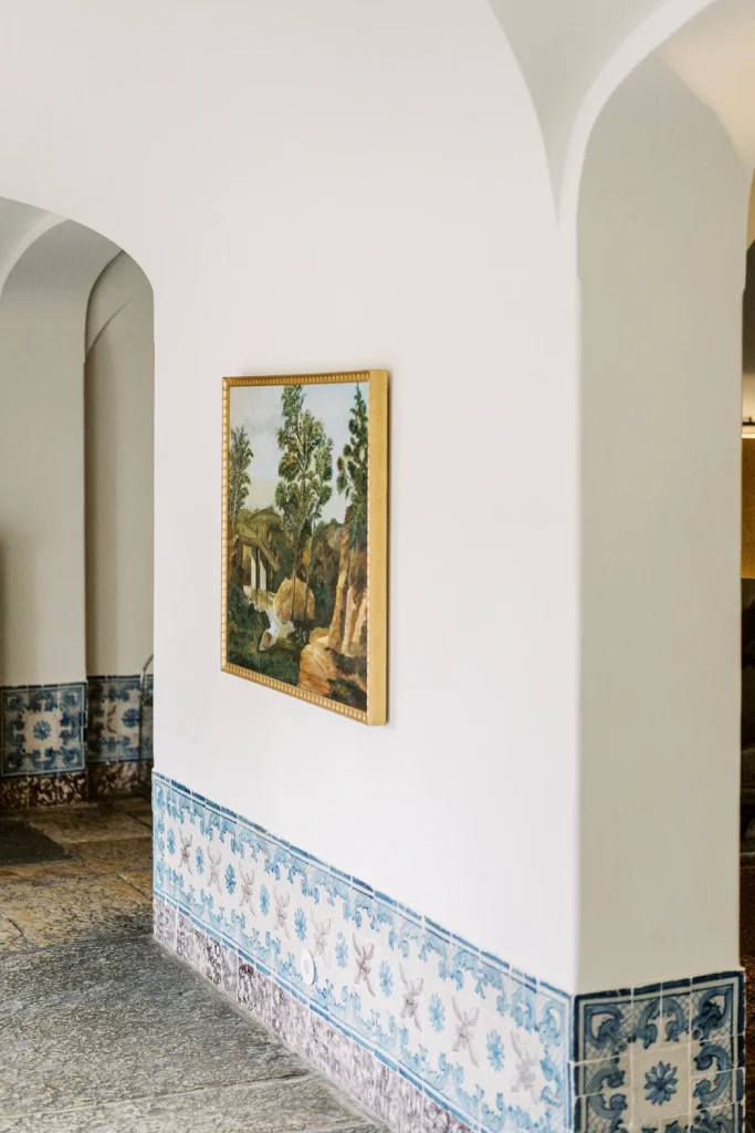 A hallway with traditional Portuguese azulejo tiles, an arched doorway, and a framed landscape painting.