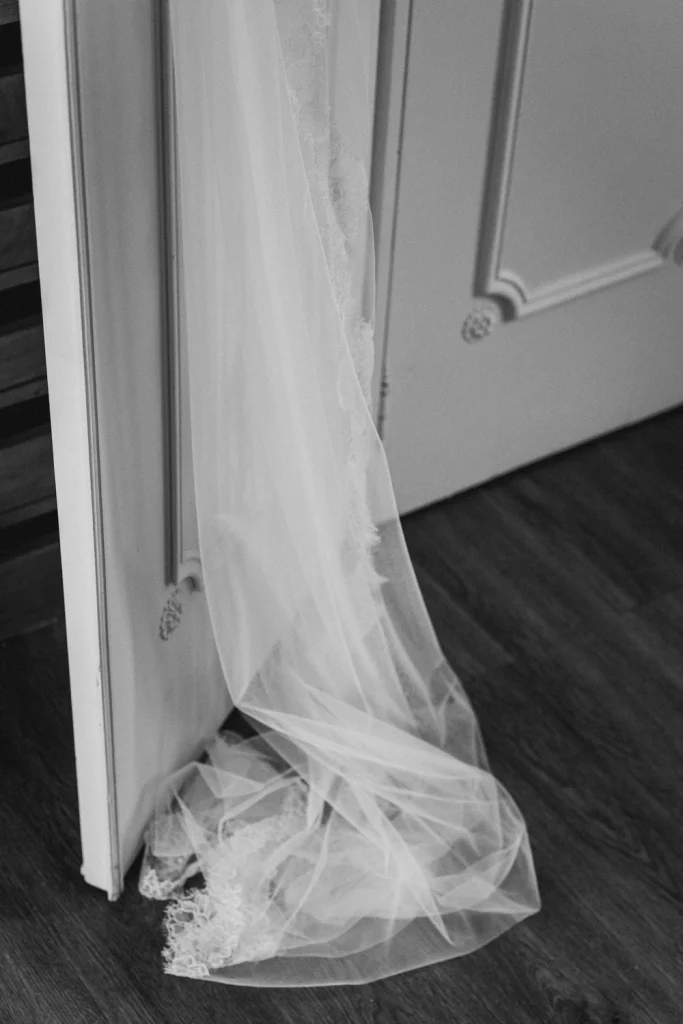 A delicate lace wedding veil cascades onto the wooden floor, draped over a white door.