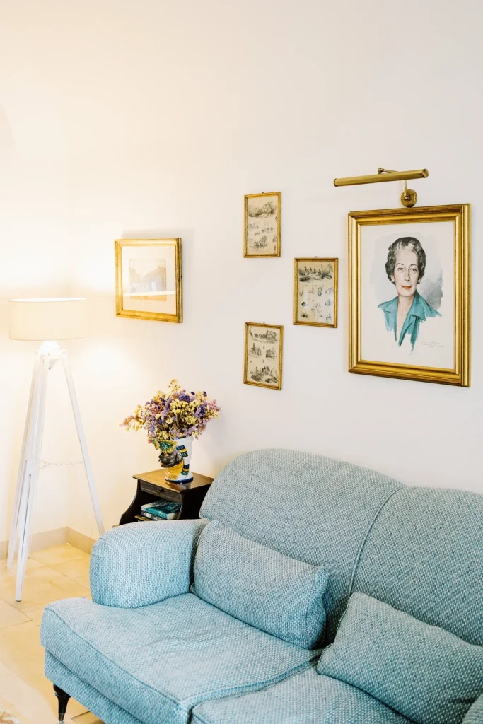 A cozy lounge room with a blue vintage sofa, framed artwork, and soft lighting, evoking a classic and elegant atmosphere.