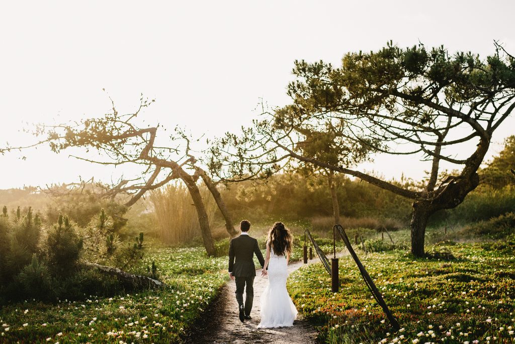A bride and groom walking into the sunset on their wedding day at Areias do Seixo, a hotel and wedding venue along the Silver Coast of Portugal
