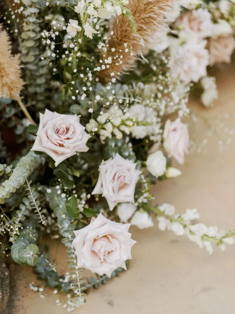 A delicate wedding floral arrangement featuring blush roses, pampas grass, and eucalyptus leaves.