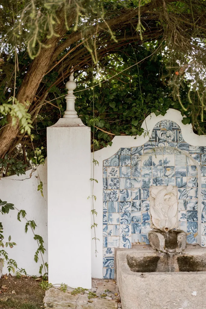 A charming Portuguese fountain with blue and white azulejo tiles, nestled under lush greenery in a garden setting.
