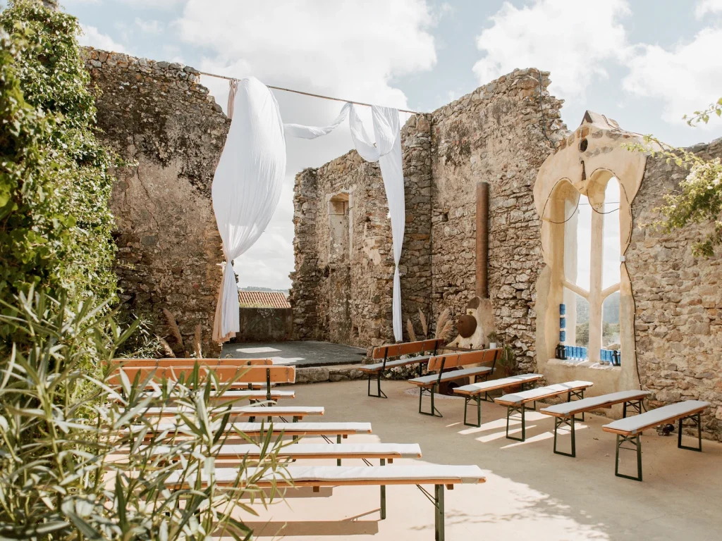 A beautifully decorated wedding ceremony setup inside historic stone ruins at Paço Dilhas, with flowing white drapery and rustic wooden benches.