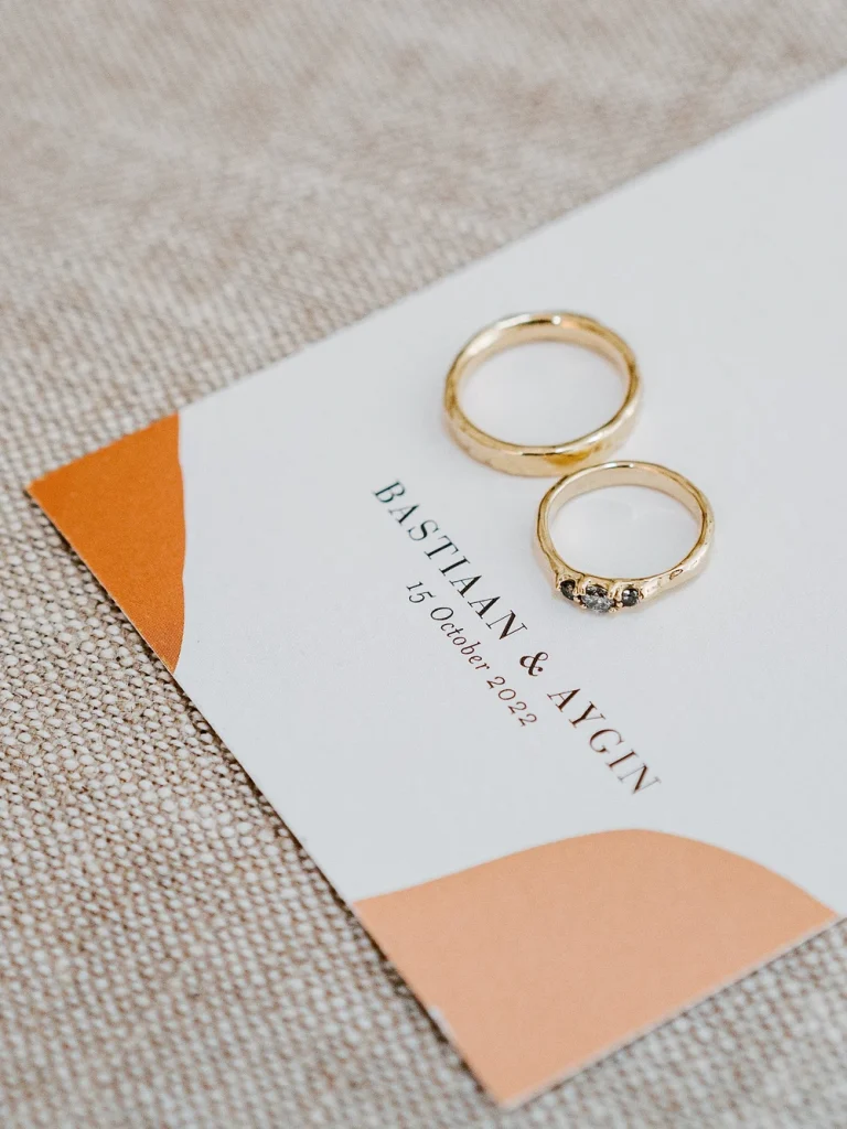 Close-up of two gold wedding rings resting on a wedding invitation with elegant typography.